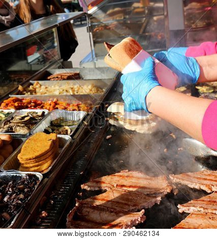 Chef With Gloves Makes A Sandwitch With Sausages In The  Stand Of Street Food In The City
