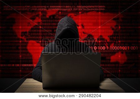 Hacker In A Jacket With A Hood With A Laptop Sits At The Table. Added Identity Theft Icons, Account 
