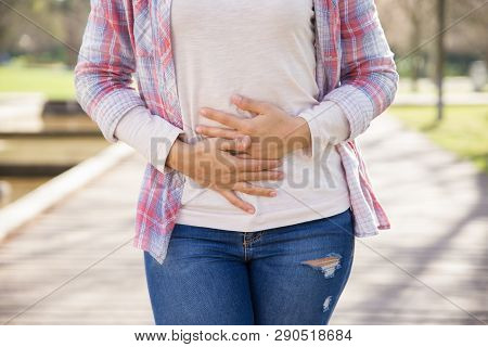 Woman Suffering From Bellyache. Cropped Portrait Of Girl Walking Outdoors And Keeping Hands On Stoma