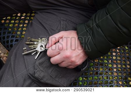 The Man Sits On A Metal Bench And Holds Key In The Hand.