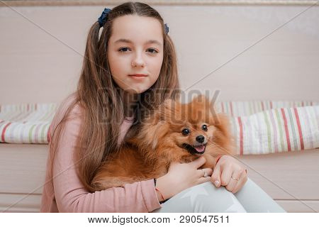 Teenage Girl With A Dog Breed Spitz Rejoices With A Pet At Home On The Floor. Care And Training Of A