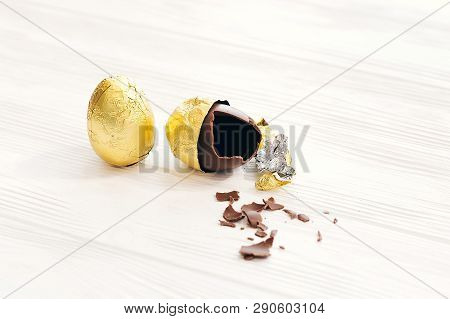 Stylish Easter Egg In Golden Foil And Broken Chocolate Egg With Chocolate Pieces On White Wooden Bac