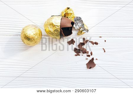 Happy Easter. Stylish Easter Egg In Golden Foil And Broken Chocolate Egg With Chocolate Pieces On Wh