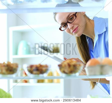 Portrait Of Female Standing Near Open Fridge Full Of Healthy Food, Vegetables And Fruits. Portrait O
