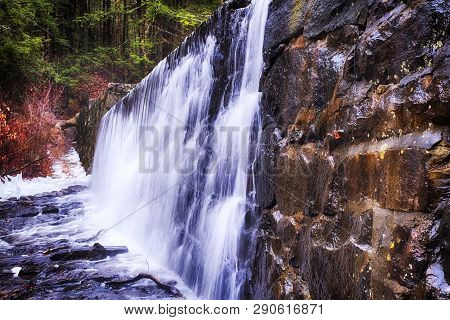 A Waterfall Flowing Over A Stone Wall At Burr Pond Torrington, Connecticut In Wintertime.