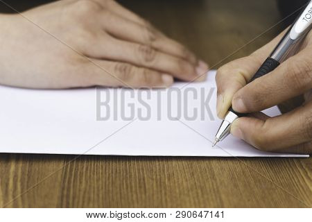 Close Up Of Woman's Hands Writing In Papr On Wooden Desktop.