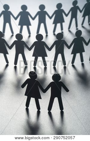 Black paper figure of a couple in front of a crowd of paper people holding hands on white surface. Social movement, protest, leadership concept.