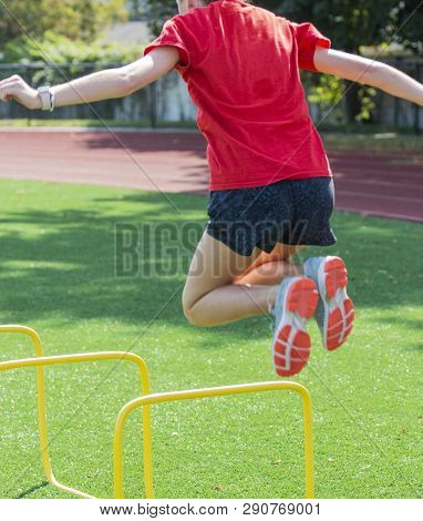 A High School Teanage Girl Is Jumping Over Two Foot High Yellow Mini Hurdels During Track And Field 