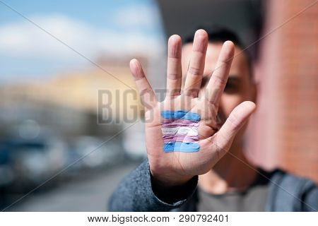 closeup of the palm of the hand of a young caucasian person with a transgender flag painted in it, in front of his or her face