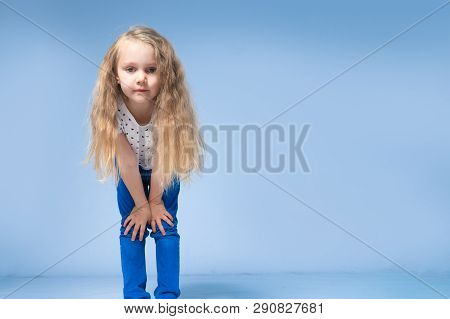 The Little Girl Leaned Forward And Looked Into The Camera With Long Blond Hair. On A Blue Background