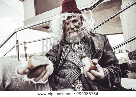 Caucasian Almsman Sitting And Eating Bun Which He Finding On The Street.