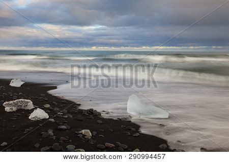 Dramatic A Sunset With Amazing Transparent Blue Iceberg Pieces On Diamond Beach With Black Sand Near