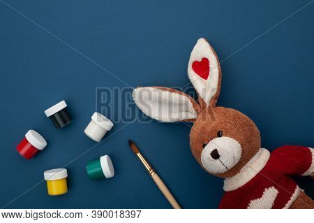 Plush Bunny On A Blue Background With Paints And A Brush