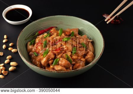 Kung Bao Chicken On A Black Background. A Chinese Dish With Chicken, Chili, Peanuts, Sauces And Onio
