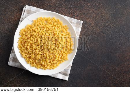 Raw Ditalini Pasta In White Plate On Brown Background. View From Above. Copy Space.