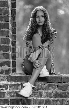 Teen Girl In Dress Sitting On Brickwork In Abandoned Place. Shallow Dof