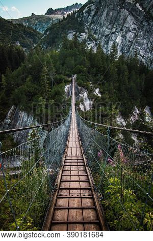 Wooden Long Footbridge Above The Deep Gorge With A River Beach At The Bottom, Between The Rocks. Wil