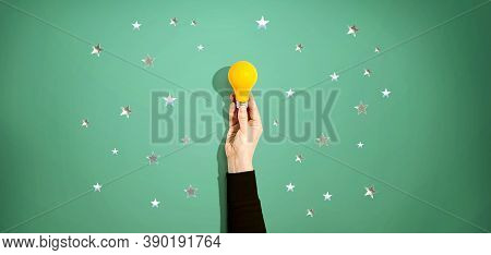 Person Holding A Yellow Light Bulb With Silver Shiny Stars