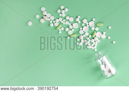 White, Green Tablets Different Sizes And Shapes Scattered From A Transparent Glass Bottle On A Mint 