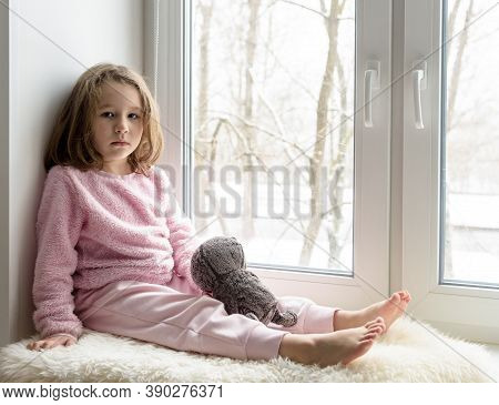Kid Sits On Windowsill At Home And Looks At Camera, Portrait Of Pretty Little Girl On Fur Rug On Roo