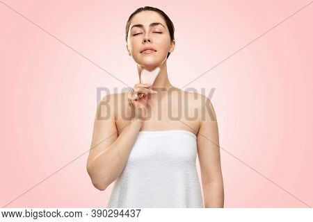 Gua Sha Massage. A Young Woman In A Bath Towel, Closing Her Eyes, Makes A Guasha Massage In The Area
