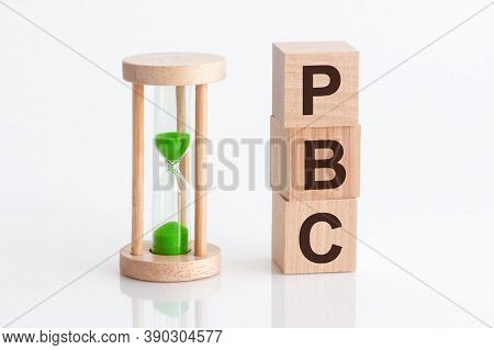 Close-up Of An Hourglass Next To Wooden Blocks With The Text Pbc