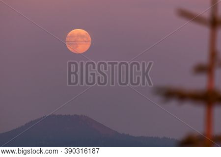 A Full Moon Rises In The East As The Sun Is Setting In The West With Thick Layers Of Smoke From A Ne