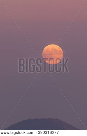 A Full Moon Rises In The East As The Sun Is Setting In The West With Thick Layers Of Smoke From A Ne