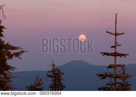 A Full Moon Rises In The East As The Sun Is Setting In The West With Thick Layers Of Smoke From A Ne