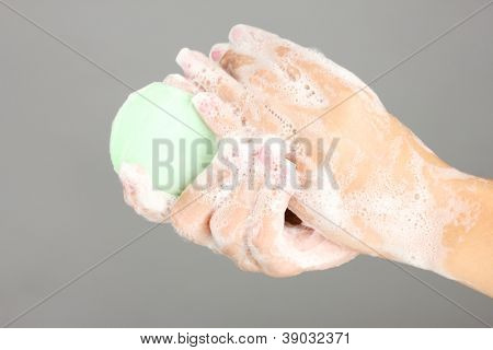 มือของผู้หญิงใน soapsuds บนพื้นหลังสีเทาอย่างใกล้ชิด