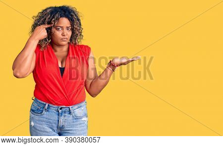 Young african american plus size woman wearing casual style with sleeveless shirt confused and annoyed with open palm showing copy space and pointing finger to forehead. think about it. 