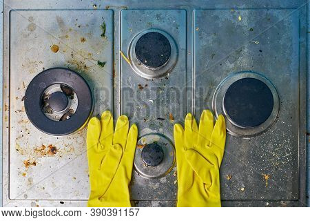 Yellow Gloves On Dirty Stove Top With Food Leftovers. Unclean Steel Kitchen Cooktop Surface With Gre