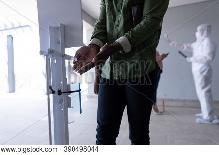 Mid sectiion of African American man sanitizing hands after health check, before entering office. Hygiene and social distancing in workplace during Coronavirus Covid 19 pandemic.