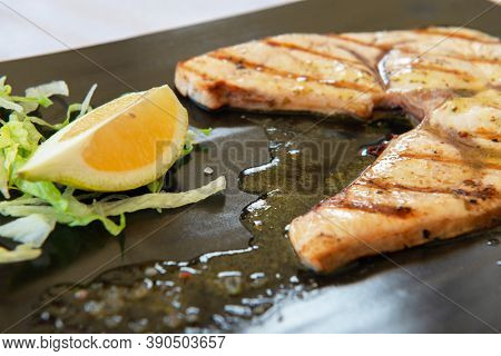Cooked swordfish. Grilled slice of fish with lemon and salsd on plate in restaurant
