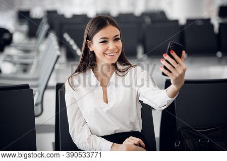 Young Business Woman At International Airport, Making Selfie With Mobile Phone And Waiting For Her F