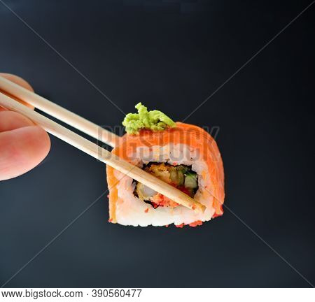 Man Holding Wooden Chopsticks Sushin, On Top Of Wasabi Sushi. Dark Background.