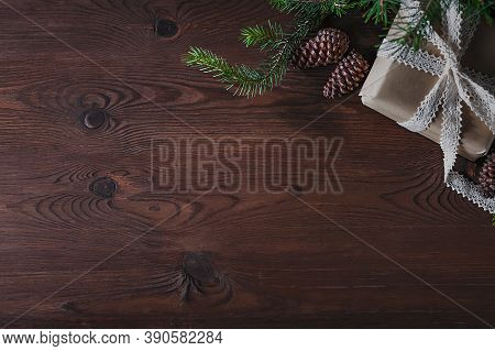 On A Wooden, Brown Background Lies A Box With A Gift, A Sprig Of A Christmas Tree And Cones.