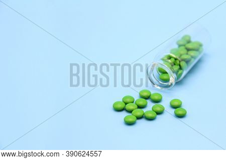 Tablets In A Green Shell, Poured Out Of A Glass Bottle On A Blue Background. Production And Packagin