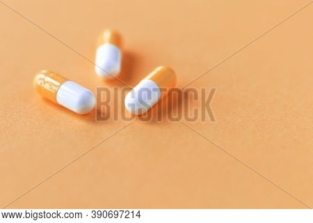 Three Orange-white Capsules On A Beautiful Pastel Orange Paper Background. Close-up, Front View. Pla