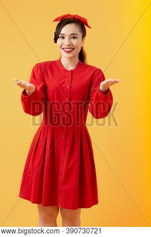 Cheerful Pretty Asian Woman In Red Dress Showing Two Brank Hands Over Orange Background.