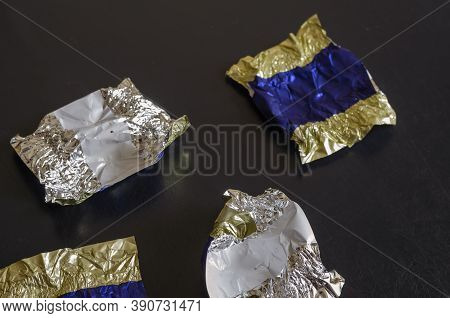 Random Blank Candy Wrappers On A Black Table. Multicolored Foil Wrappers With Crumbs And Spots. Choc