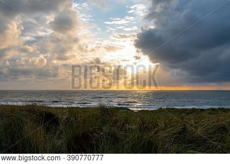 Sunset On The North Sea Near The Town Of Petten, With Dark Colored Clouds And An Orange Setting Sun