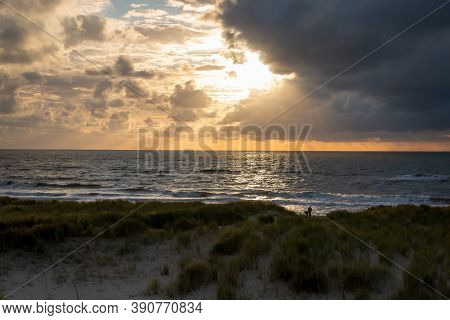 Sunset On The North Sea Near The Town Of Petten, With Dark Colored Clouds And An Orange Setting Sun