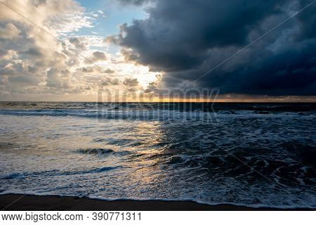 Sunset On The North Sea Near The Town Of Petten, With Dark Colored Clouds And An Orange Setting Sun