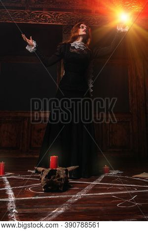 A portrait of a scary witch holding a magic glowing ball in her hand in the wooden house. Magic, dark force, spell. 