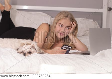Beautiful Blonde With A Puppy Shih-tzu And Laptop On Bed With White Sheets. Pretty People And Pets O