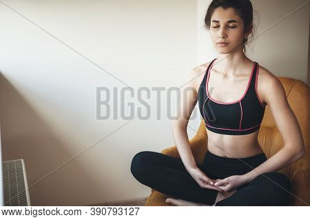 Brunette Woman In Sportswear Is Meditating On Chair At Home Near Free Space