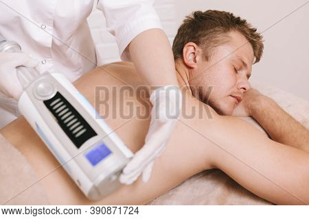 Young Man Relaxing At Beauty Salon While Beautician Using Endospheres Massage Device On His Back. Re
