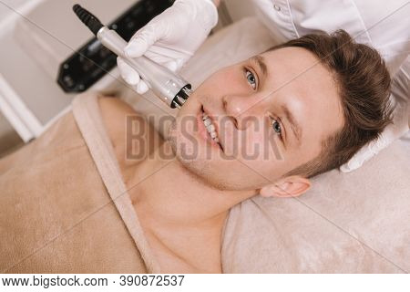 Cheerful Handsome Man Smiling While Getting Hardware Skincare Treatment By Cosmetologist