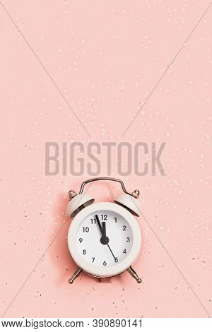 White Alarm Clock Shows About Twelve Oclock On Pink Paper Background Covered With Sequins With Copy 